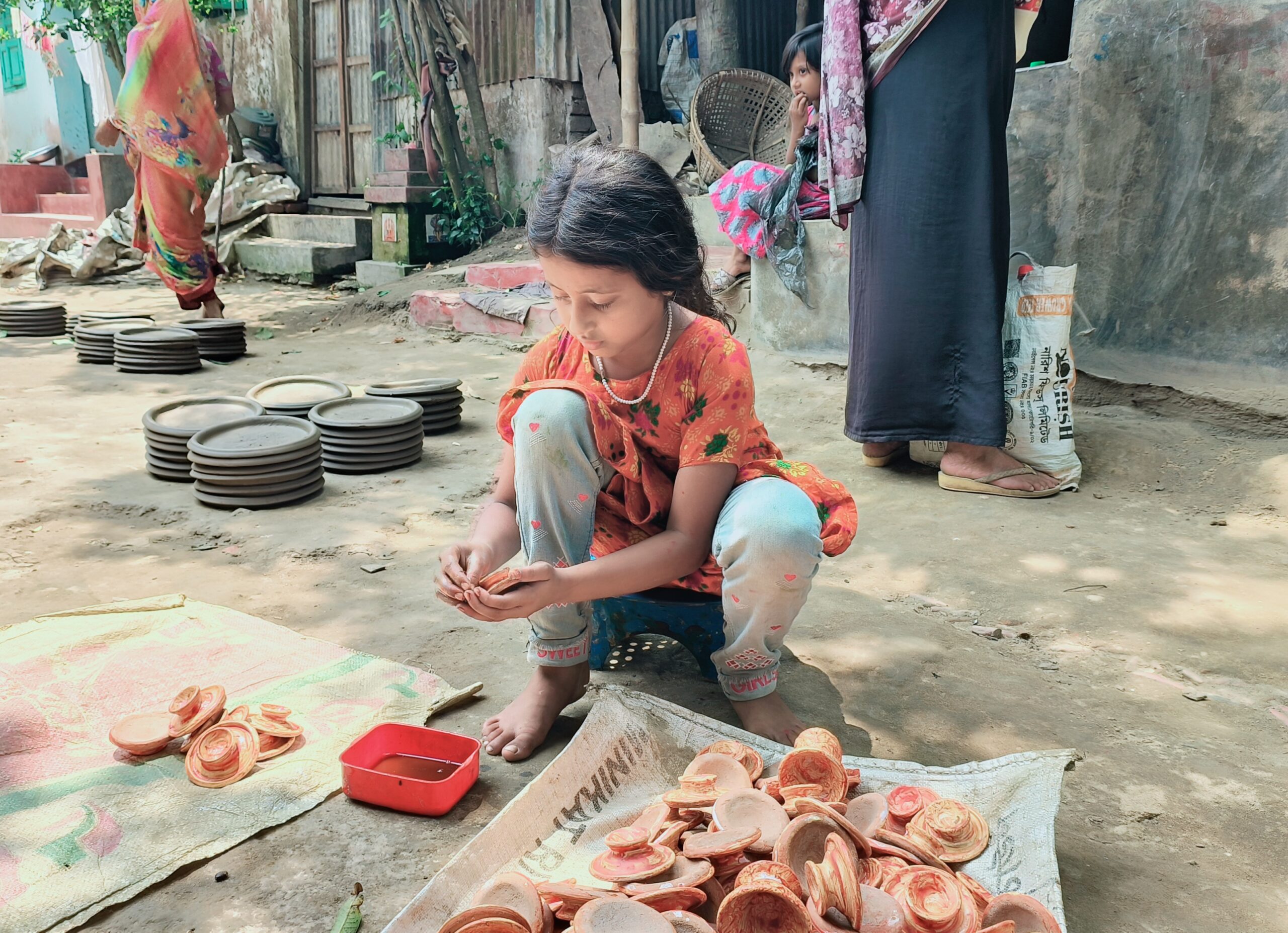 মৃৎশিল্পী বাবার মাটির তৈরি পণ্যে রং তুলির আঁচড় দিচ্ছেন স্নেহা